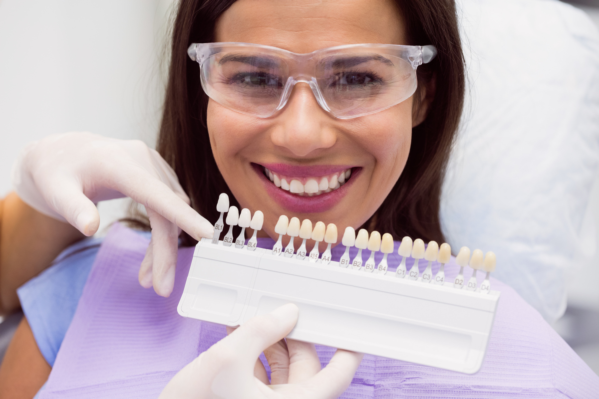 Dentist examining female patient with teeth shades at dental clinic Відбілювання зубів в Одесі